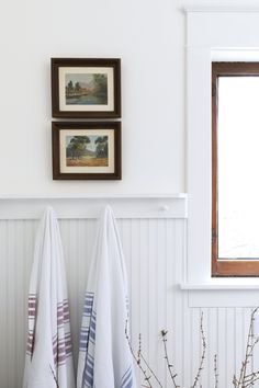 two white towels hanging on the wall next to a window with framed pictures above it