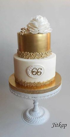 a three tiered cake with gold trim and white flowers on the top, sitting on a pedestal