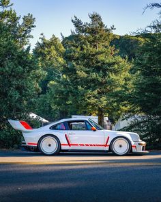 a white car with red stripes parked on the side of the road near some trees