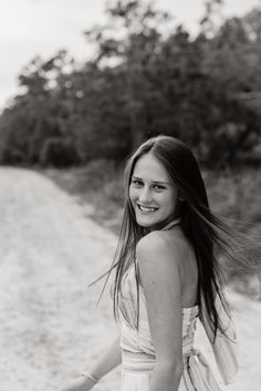 black and white photograph of woman in dress on dirt road with trees in the background