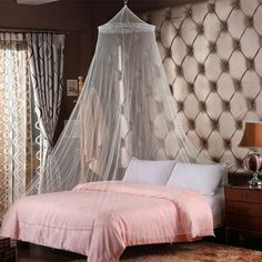 a bed with a white net hanging over it's head and pillows on the floor