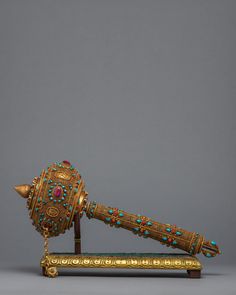 an ornately decorated golden object with beads on it's end and a wooden stand