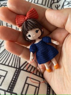 a hand holding a tiny crocheted doll in it's left hand,