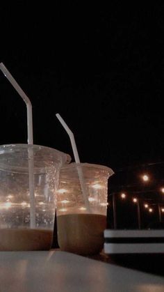 three plastic cups with straws are lined up on a table in front of some lights