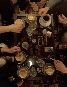 four people sitting at a table with cups of coffee in front of them and one person holding a spoon