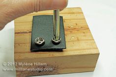 a hand holding a pen over a wooden block with two metal rings on the end