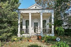 a small white house sitting in the middle of a yard with trees and bushes around it