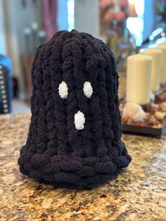 a crocheted black hat with white eyes and nose on a marble counter top