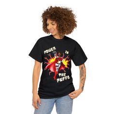 Not available in stores. Take your style to new heights with this Power in the Puffs tee. This unisex heavy cotton tee is perfect for anyone who wants to show off their superhero style. The shirt features a bold print of the iconic Afro Puff Superhero on the front, making it a must-have for any fan of Black Superheroines. Whether you're wearing it to the gym or out on the town, this tee is sure to turn heads and get you noticed. So power up and put your best foot forward in this stylish Superher Superhero Cotton Tops For Streetwear, Superhero Graphic T-shirt For Fans, Superhero Graphic T-shirt For Streetwear, Black Superhero Fan Merchandise T-shirt, Black Superhero T-shirt With Graphic Print, Superhero Graphic T-shirt Fan Merchandise, Superhero Cotton T-shirt With Graphic Print, Superhero Fashion, Afro Puff