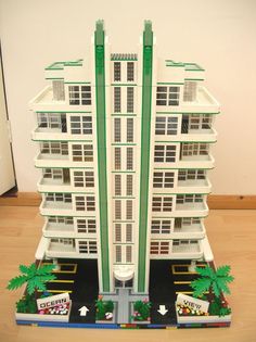 a model of a building with palm trees on the ground and cars parked in front of it