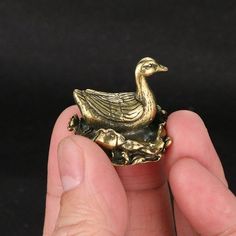 a gold duck figurine sitting on top of a piece of wood in someone's hand