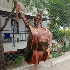 a backpack hanging on a chain link fence in front of a building with a tree growing out of it