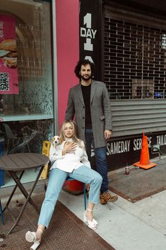 a man standing next to a woman sitting on a chair in front of a store