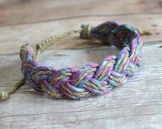 a multicolored braid bracelet sitting on top of a wooden table next to a piece of string