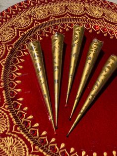 four gold colored pens sitting on top of a red and gold tablecloth with intricate designs