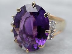 The focal point of this ring is absolutely the outstanding eggplant-colored amethyst that we've set at the center. Sparkling accent diamonds light up the shoulders, bringing even more glitz and glamor to this beautiful gem! Metal: 14K Yellow Gold Gem: Amethyst 5.88 Carats Gem Measurements: 15.2 x 11.7 mm, Oval Accents: 6 Diamonds totaling .18 Carats, VS in Clarity, G in Color Ring Size: 8 SKU #: A11567 Each piece has been identified and graded by a Graduate Gemologist who has been certified by t Luxury 14k Gold Hallmarked Amethyst Ring, Luxury Multi-stone Amethyst Ring In Yellow Gold, Luxury Gold Amethyst Multi-stone Ring, Antique Gold Amethyst Multi-stone Ring, Gold Amethyst Ring, Fine Jewelry Collectible, Amethyst Cocktail Ring, Purple Stone Rings, White Gold Sapphire, Black Hills Gold