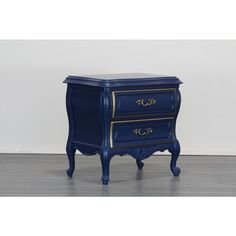 a blue nightstand with gold trimmings on the top and bottom drawers, in front of a white wall