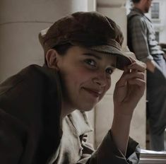 a woman sitting at a table with a hat on her head and another man standing in the background