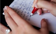 a person writing on a piece of paper with a red pen in their left hand