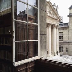 an open window with books on the shelves in front of it and a building behind it