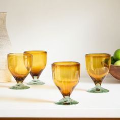 four yellow glass goblets sitting on a table next to a vase and apples