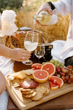 a man pouring wine into a glass next to a tray of cheese, fruit and crackers