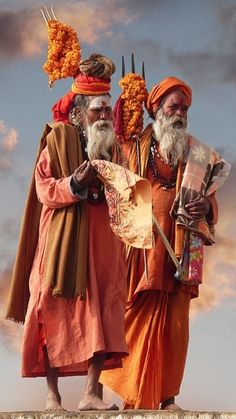 two men dressed in orange standing next to each other on top of a stone wall