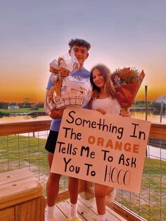 a man and woman standing on a wooden deck holding signs that say something in the orange tells me to ask you to go