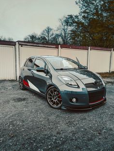 a small gray car parked next to a white fence