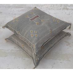 a gray pillow with an embroidered design on the front and back, sitting on concrete