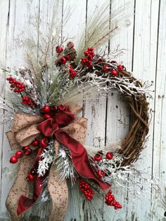 a wreath with red berries and greenery is hanging on a white wooden wall,