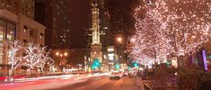 a city street filled with lots of lights and trees covered in white christmas lights next to tall buildings