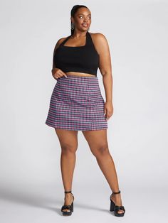 a woman in a black top and plaid skirt poses for the camera with her hands on her hips