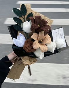 a bouquet of crocheted flowers is being held by someone's hand on the street