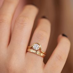 a woman's hand holding a gold ring with a diamond in it and the band on her finger