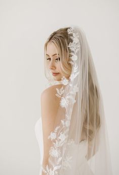 a woman wearing a wedding veil with white flowers on the side and long hair in front