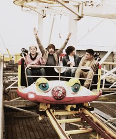 four people riding on a roller coaster with their arms in the air and eyes painted on them