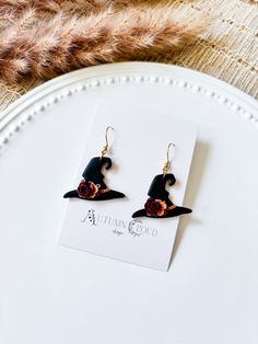 a pair of earrings with a black hat and rose on it sitting on top of a white plate