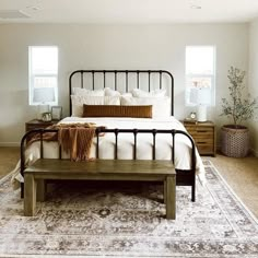 a bedroom with a large bed and two windows in the corner, along with a rug on the floor