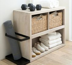 a wooden shelf with baskets, towels and shoes next to a wall mounted towel dispenser