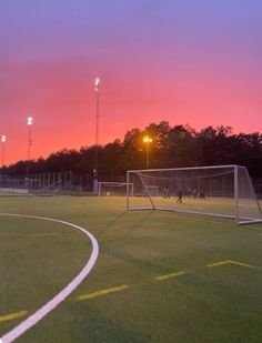 a soccer field at sunset with the goal in the foreground and people playing on the other side