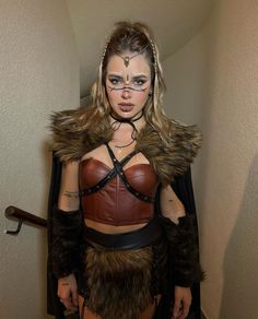 a woman dressed up as a warrior with fur and leather on her shoulders, standing in a hallway