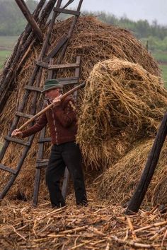 a man with a stick standing next to a pile of hay