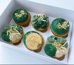 six cupcakes in a white box with green frosting and gold decorations on them