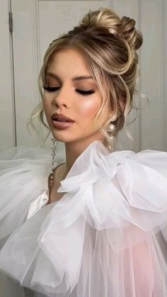 a woman with blonde hair wearing a white dress and large earrings, looking down at the camera