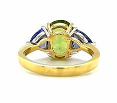 The sophisticated color pairing of green peridot and rich tanzanites in this elegant ring is absolutely mesmerizing! We have combined a gorgeous 3.62 carat brilliant peridot oval with two sparkling trilliant-cut tanzanites in this updated version of a classic three-stone ring. The vibrant "Granny Smith" green peridot looks stunning perched between the unmistakable purple-blue color of the tanzanites. A rich statement of everyday elegance and creative style, this ring is perfect for both daytime Green Oval Sapphire Ring With Center Stone, Oval Multi-stone Peridot Gemstones, Green Tanzanite Multi-stone Jewelry, Oval Tsavorite Multi-stone Ring, Oval Multi-stone Tsavorite Rings, Oval Green Multi-stone Gemstones, Green Oval Multi-stone Gemstones, Green Oval Sapphire Ring For Formal Occasions, Formal Green Multi-stone Sapphire Ring