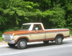 an orange and white truck is parked on the side of the road in front of some trees