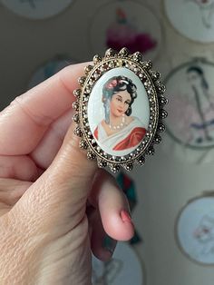 Embrace the elegance and artistry of French craftsmanship with this exquisite Vintage Limoges Brooch, a handpainted cameo that epitomizes the beauty and sophistication of vintage costume jewelry. This stunning brooch features a delicate cameo design, meticulously handpainted on fine porcelain, showcasing the exceptional skill and attention to detail that Limoges is renowned for. The cameo depicts a classical portrait, rich in detail and beautifully rendered in soft, delicate colors. The fine brushstrokes and intricate design highlight the artisan's craftsmanship, making this brooch a true work of art. The porcelain cameo is set in an elegant frame with faux pearls, adding a touch of luxury and complementing the delicate artwork. Limoges, a region in France famous for its high-quality porce Luxury Elegant Intaglio Brooch, Vintage Intaglio Brooches Gift, Vintage White Cameo Brooches, Limoges Pendant, Limoges France Painted Porcelain, French Jewelry, Elegant Frame, Cameo Brooch, Porcelain Jewelry