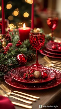 a christmas table setting with candles, plates and red glassware on top of a wooden table