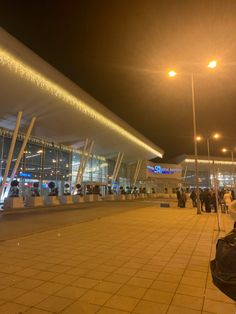 many people are standing outside at night with their suitcases in front of the terminal